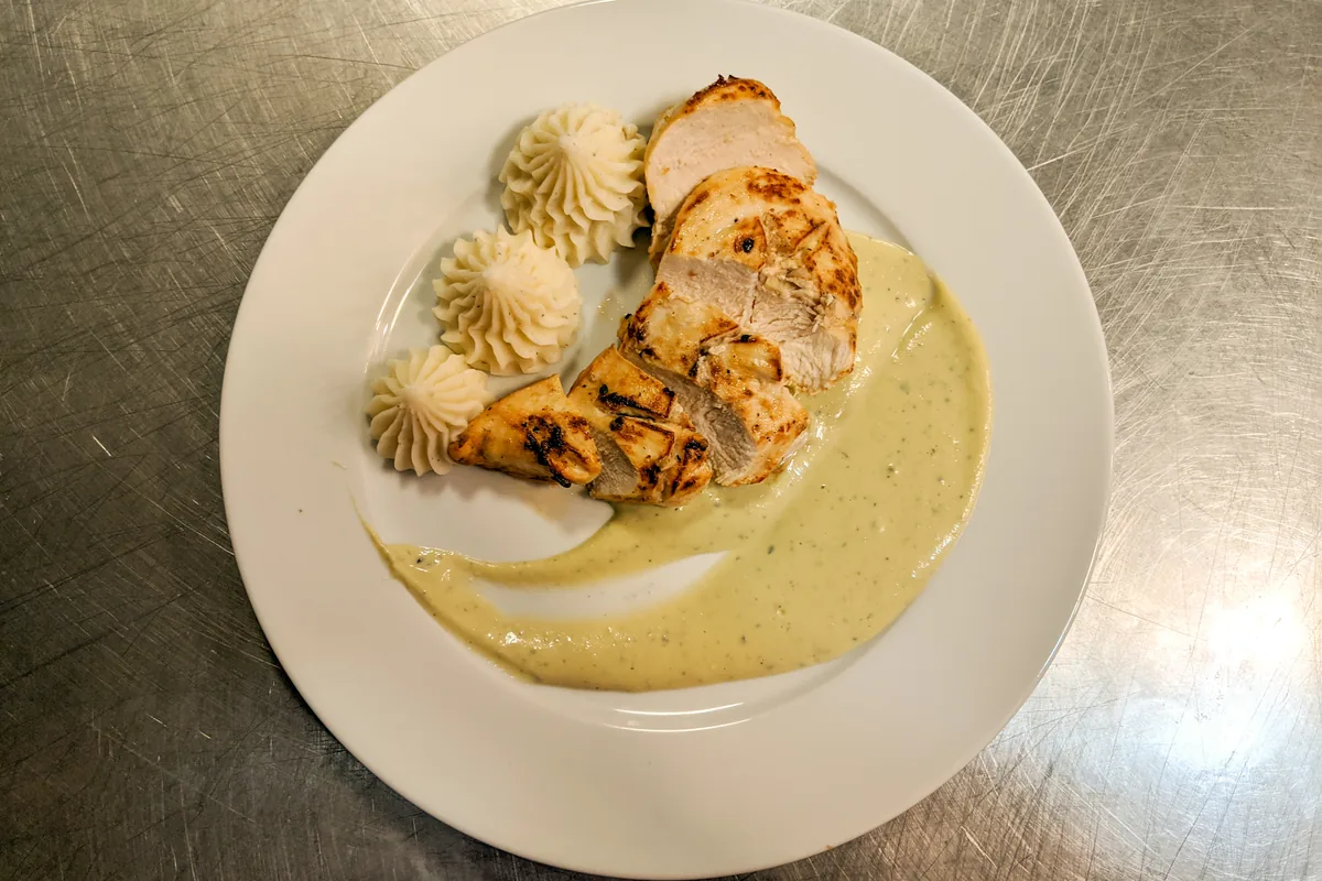 Chicken Steak with Blue Cheese Sauce Sliced Chicken Steak with Blue Cheese Sauce on a white plate with piped mashed potato swirls.