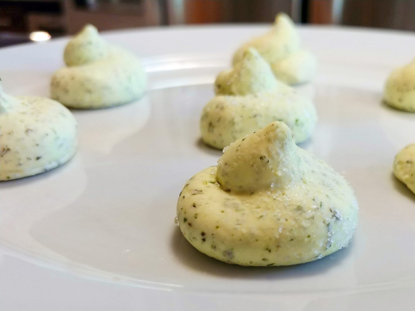 Herb Butter Small dollops of pale green Herb Butter with herb flecks arranged on a white ceramic plate.