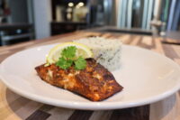 Blackened Salmon fillet with a lemon wedge and herb garnish beside herbed rice on a white plate