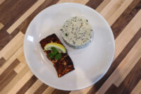 Blackened Salmon fillet with lemon wedge and herb garnish beside a mound of rice on a white plate
