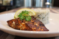 Blackened Salmon fillet on a plate with herbed rice, lemon wedge, and parsley garnish