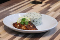 Blackened Salmon fillet with a lemon wedge and herb sprig beside herbed white rice on a plate.