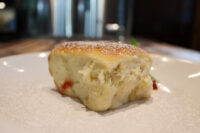 Buchty – Czech Sweet Filled Buns A golden Buchty (Czech sweet filled bun) dusted with powdered sugar, red filling visible at its base, on a white plate.