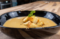 Bowl of Cauliflower Soup topped with golden croutons and a parsley sprig, on a wooden table