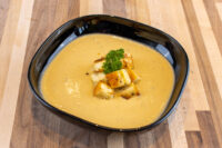 A black bowl of creamy Cauliflower Soup topped with golden croutons and a parsley sprig.
