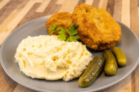 Dutch Schnitzel (Holandský Řízek) Two golden breaded Dutch Schnitzel (Holandský Řízek) cutlets on a grey plate with mashed potatoes and pickles.