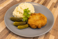 Dutch Schnitzel (Holandský Řízek) Golden breaded Dutch Schnitzel (Holandský Řízek) on a gray plate with mashed potatoes and gherkins.