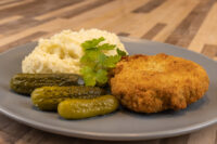 Dutch Schnitzel (Holandský Řízek) Golden breaded Dutch Schnitzel (Holandský Řízek) with mashed potatoes, pickles, and parsley on a gray plate