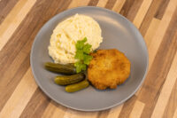 Dutch Schnitzel (Holandský Řízek) Golden breaded Dutch Schnitzel (Holandský Řízek) on a gray plate with mashed potatoes, pickles, and parsley.