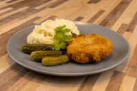 Dutch Schnitzel (Holandský Řízek) Golden breaded Dutch Schnitzel (Holandský Řízek) plated with mashed potatoes, cornichons, and parsley.