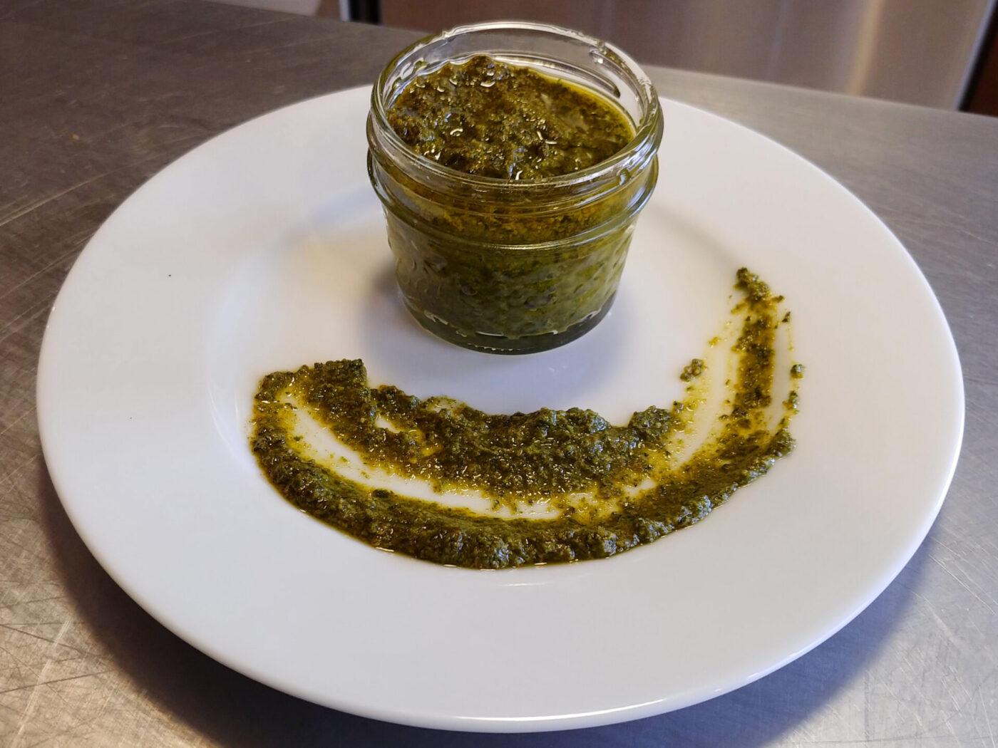 Pesto in Jar A glass jar of pesto beside a swirl of the same green sauce on a white plate.