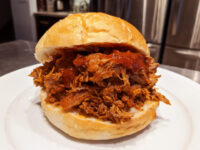 Pulled pork Pulled pork sandwich with red BBQ sauce on a soft bun, served on a white plate.