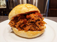 Pulled pork Pulled pork piled high in a bread roll with red barbecue sauce, on a white plate