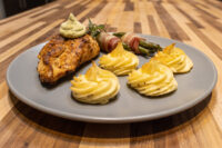 Rosemary Chicken Breasts Seared Rosemary Chicken Breasts with herb sauce, duchess potatoes, and bacon-wrapped asparagus on a grey plate.