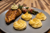Rosemary Chicken Breasts Seared Rosemary Chicken Breasts topped with herb cream, rosemary sprig, potatoes and asparagus on grey plate