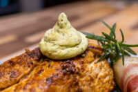 Rosemary Chicken Breasts Seared Rosemary Chicken Breast topped with green herb butter, rosemary sprig and cured meat curl alongside.