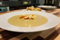 Broccoli Soup A white bowl of pale, creamy Broccoli Soup topped with golden croutons on a wooden table.