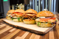 Burger Buns Four sesame-seed Burger Buns filled with patties, tomato, onion and greens on a wooden board.