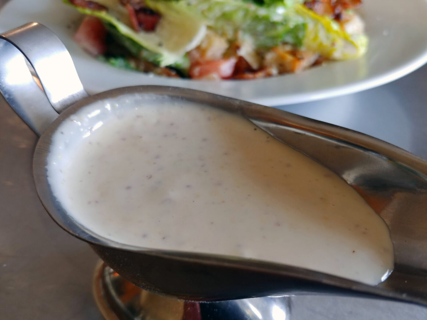 Caesar Dressing (easy version) Creamy Caesar Dressing (easy version) pooled in a metal sauce boat, salad blurred behind it.