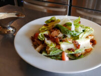 Caesar Salad White plate of Caesar Salad with romaine leaves, croutons, shaved cheese, and diced tomato.