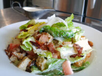 Caesar Salad with Bacon Caesar Salad with romaine, bacon, croutons, shaved cheese, and a gravy boat of dressing.