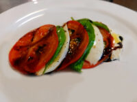 Caprese Salad Sliced tomato and mozzarella fanned with basil, drizzled with balsamic glaze, plated as Caprese Salad