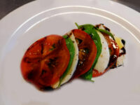 Caprese Salad Caprese Salad with layered tomato and mozzarella slices, basil leaves, and balsamic drizzle on a white plate.