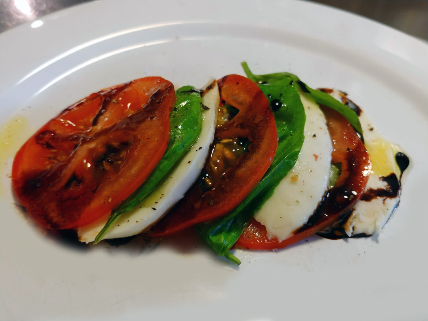 Caprese Salad Caprese Salad with overlapping tomato and mozzarella slices, basil leaves, and a balsamic glaze drizzle on a white plate.