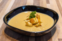 Bowl of Cauliflower Soup topped with crispy croutons and a parsley garnish on a wooden table.
