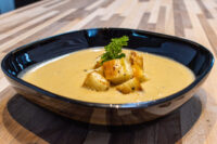 Bowl of Cauliflower Soup topped with golden croutons and a parsley sprig on a wooden table