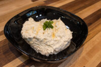 Cheese – Garlic Dip and Spread Cheese – Garlic Dip and Spread mounded in a black bowl with visible corn kernels and a parsley sprig.