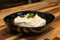 Cheese – Garlic Dip and Spread Cheese – Garlic Dip and Spread mounded in a dark oval bowl, topped with a parsley sprig, on a wooden counter.