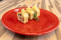 Three sliced pieces of Cheese Roulade with Goat Cheese & Raisins topped with piped cream on a red plate.