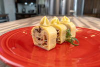 Three sliced rounds of Cheese Roulade with Goat Cheese & Raisins on a red plate with a herb sprig