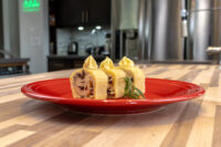 Sliced rounds of Cheese Roulade with Goat Cheese & Raisins topped with piped garnish on a red plate