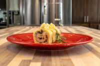Sliced Cheese Roulade with Goat Cheese & Raisins on a red plate, garnished with piped cream and a herb sprig.