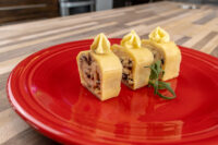 Three sliced rounds of Cheese Roulade with Goat Cheese & Raisins topped with piped cream on a red plate.