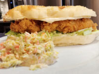 Coleslaw Bowl of creamy Coleslaw with shredded cabbage and carrot, served alongside a fried chicken sandwich.