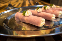 Creamy Horseradish Ham Rolls Four Creamy Horseradish Ham Rolls piped with white cream and topped with herb garnish, arranged on a shiny metal platter.