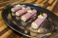 Creamy Horseradish Ham Rolls Four Creamy Ham Rolls piped with white filling and garnished with parsley, arranged on an oval metal platter atop a wooden table