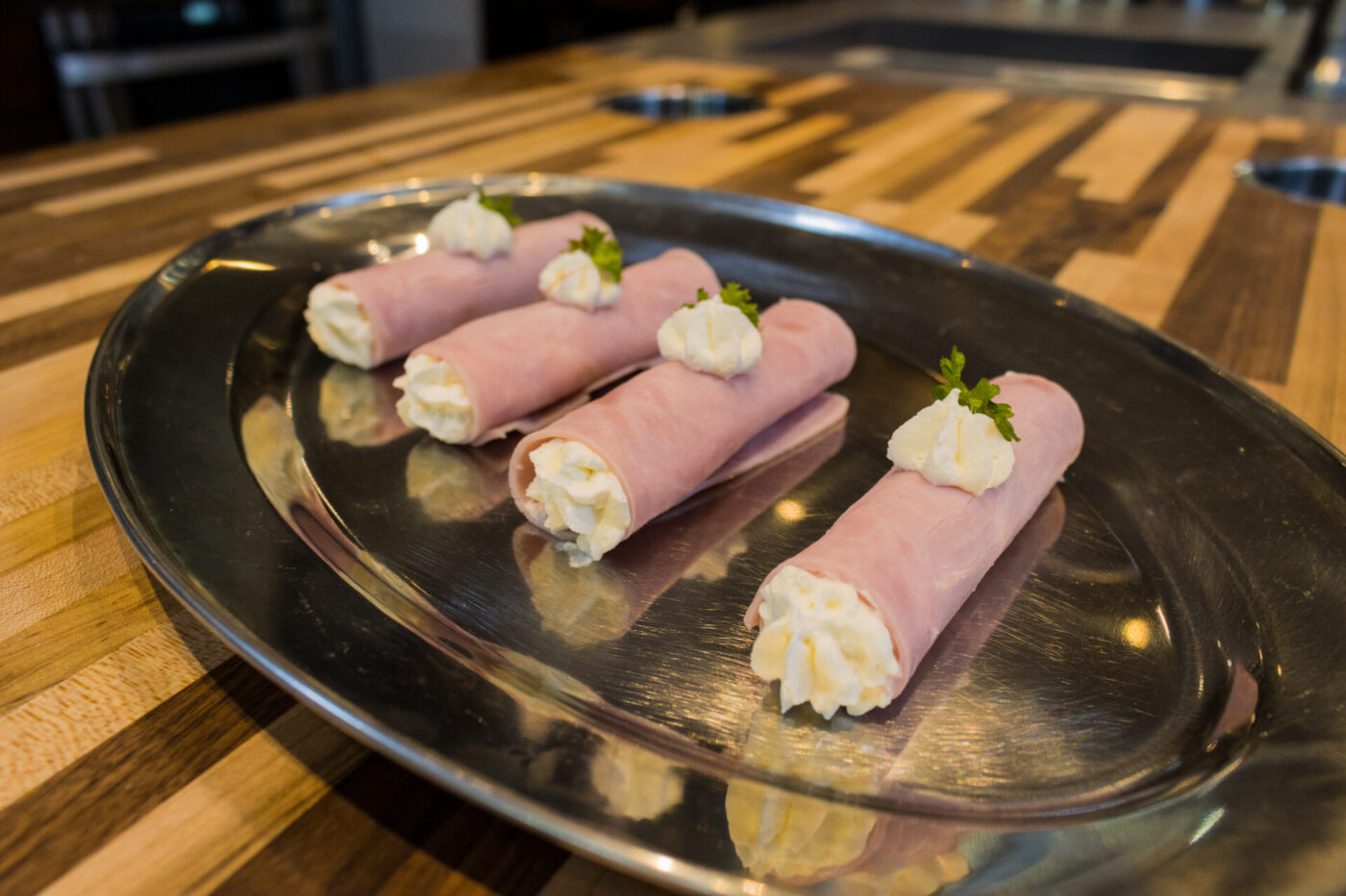 Creamy Horseradish Ham Rolls Six Creamy Ham Rolls piped with white cream filling and garnished with parsley, arranged on a round metal plate.