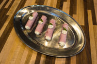 Creamy Horseradish Ham Rolls Four Creamy Horseradish Ham Rolls piped with white cream and garnished with herb leaves on a metal tray.