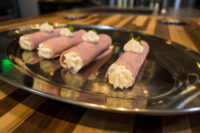 Creamy Horseradish Ham Rolls Four Creamy Ham Rolls piped with white filling and topped with herb leaves, arranged on a metal tray.