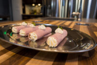Creamy Horseradish Ham Rolls Four Creamy Horseradish Ham Rolls piped with cream filling and herb garnish on a metal platter.