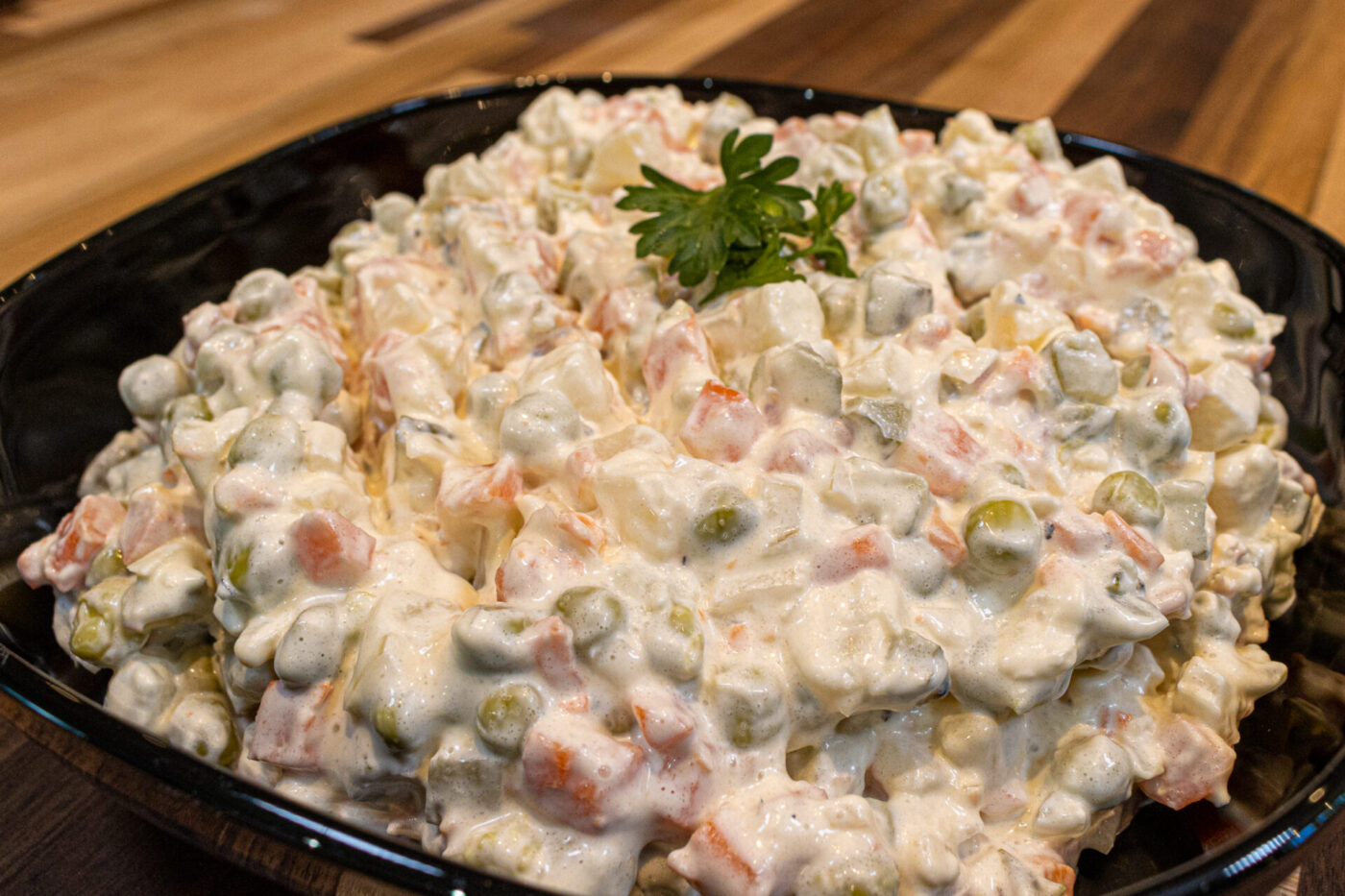 Bowl of Vlašský Salát Vlašák with diced potato, carrot, peas, and creamy dressing, garnished with parsley.