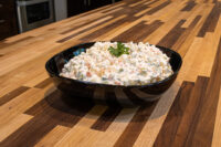 Black bowl of Vlašský Salát Vlašák with diced carrot, potato, and peas, topped with parsley, on a wood counter.