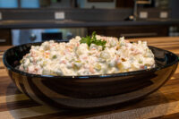 Bowl of Vlašský Salát Vlašák Czech deli salad with peas, carrot, and pickles, garnished with parsley.