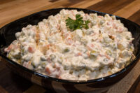 Bowl of Vlašský Salát Vlašák with peas, carrots, and diced potato in creamy dressing, garnished with parsley.