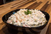 Bowl of Vlašský Salát Vlašák with diced potatoes, carrots, peas, and mayonnaise, topped with parsley.
