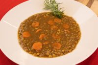 Bowl of Czech Lentil Soup Čočková Polévka with sliced carrots, garnished with a green herb sprig.